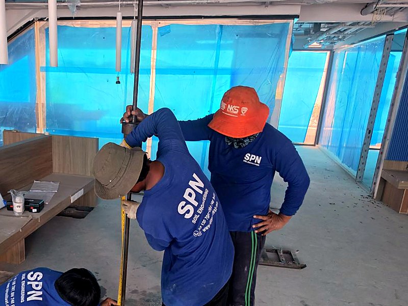 ทีมช่างเทคนิค SPN สามคนทดสอบ Kunzelstab ตอกก้านเหล็กลงในดินผ่านรูเจาะในพื้นคอนกรีตและอ่านระยะจมด้วยตลับเมตร