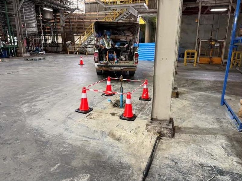 ท่อ PVC สำหรับทดสอบ Parallel Seismic ฝังข้างฐานรากเสาอาคารในโรงงาน ล้อมด้วยกรวยจราจรและเทปกั้น สายสัญญาณต่อไปยังรถทดสอบด้านหลัง
