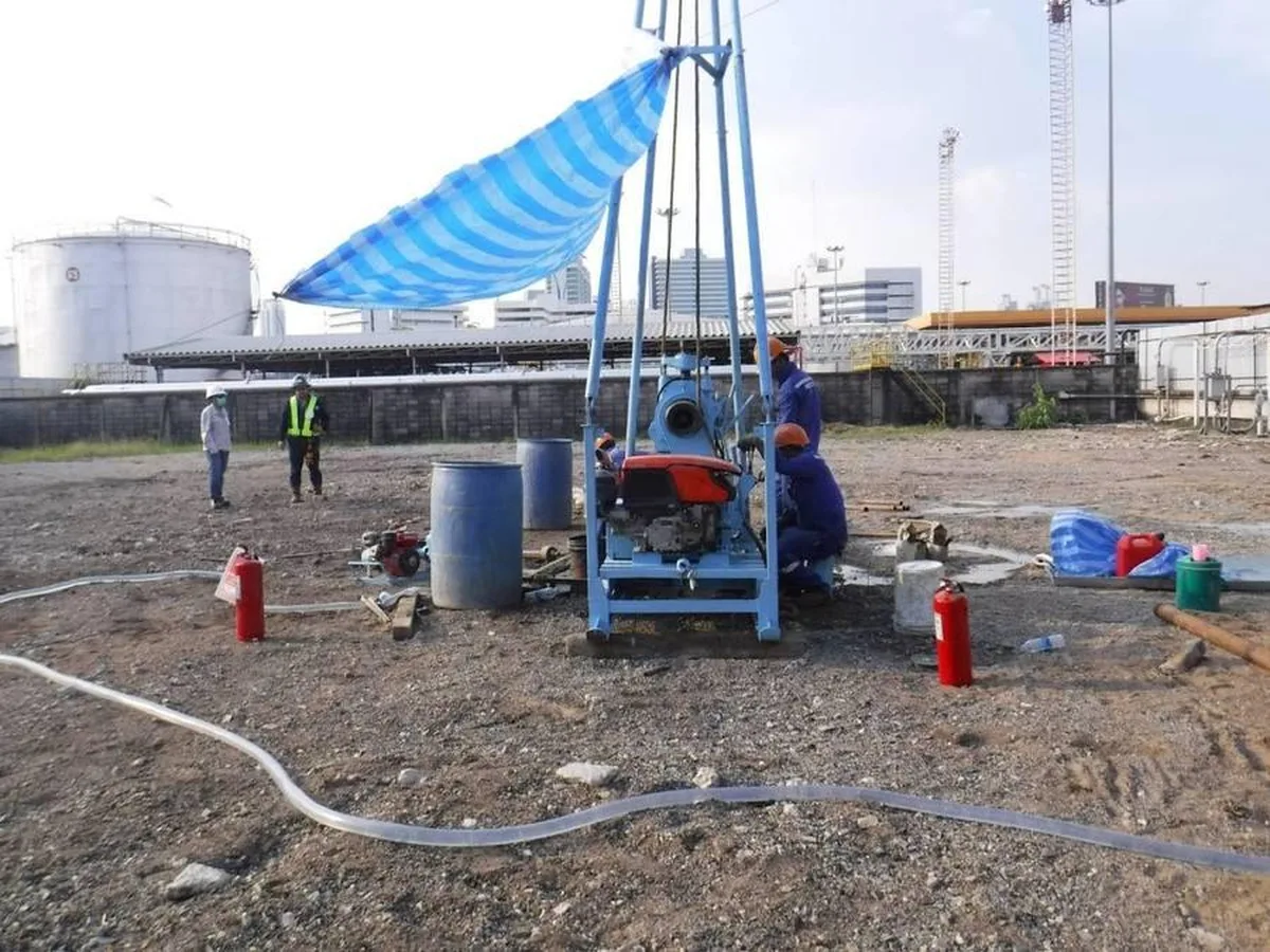 เครื่องเจาะสำรวจดินแบบหมุน (Rotary Drilling) ติดตั้งบนฐานเหล็กในพื้นที่คลังน้ำมัน มีทีมงานควบคุมเครื่อง
