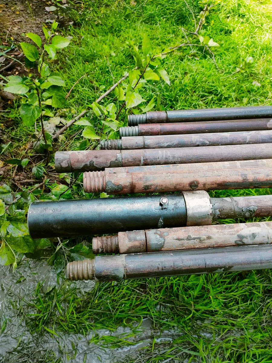 ก้านเจาะเหล็ก (Drill Rods) หลายท่อนพร้อมกระบอกเก็บตัวอย่างดิน วางเรียงบนพื้นหญ้าข้างจุดเจาะ