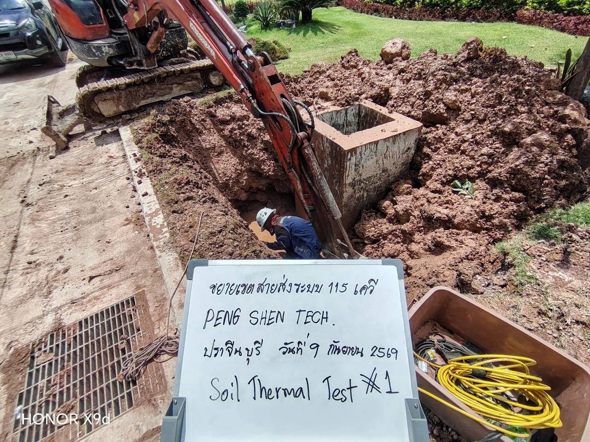 มุมกว้างของหลุมทดสอบจุดที่ 1 เห็นรถขุด กองดินลูกรังที่ขุดขึ้นมา และกล่องเครื่องมือทดสอบ Soil Thermal Conductivity พร้อมสายวัดสีเหลือง