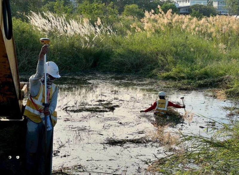 ช่างสำรวจ SPN ถือเสารับสัญญาณ GNSS ขณะเพื่อนร่วมทีมลุยน้ำลึกเก็บค่าระดับในพื้นที่ลุ่มน้ำท่วมขัง